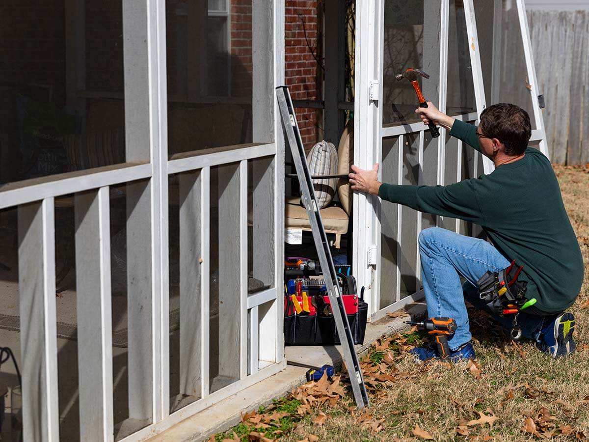 Worker installing screened in porch at exterior of renovation home